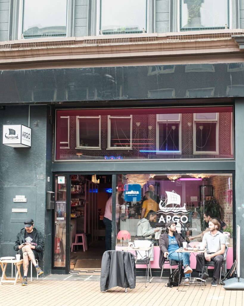 De gevel en het terras van de roze Griekse koffiebar Argo aan de Herestraat