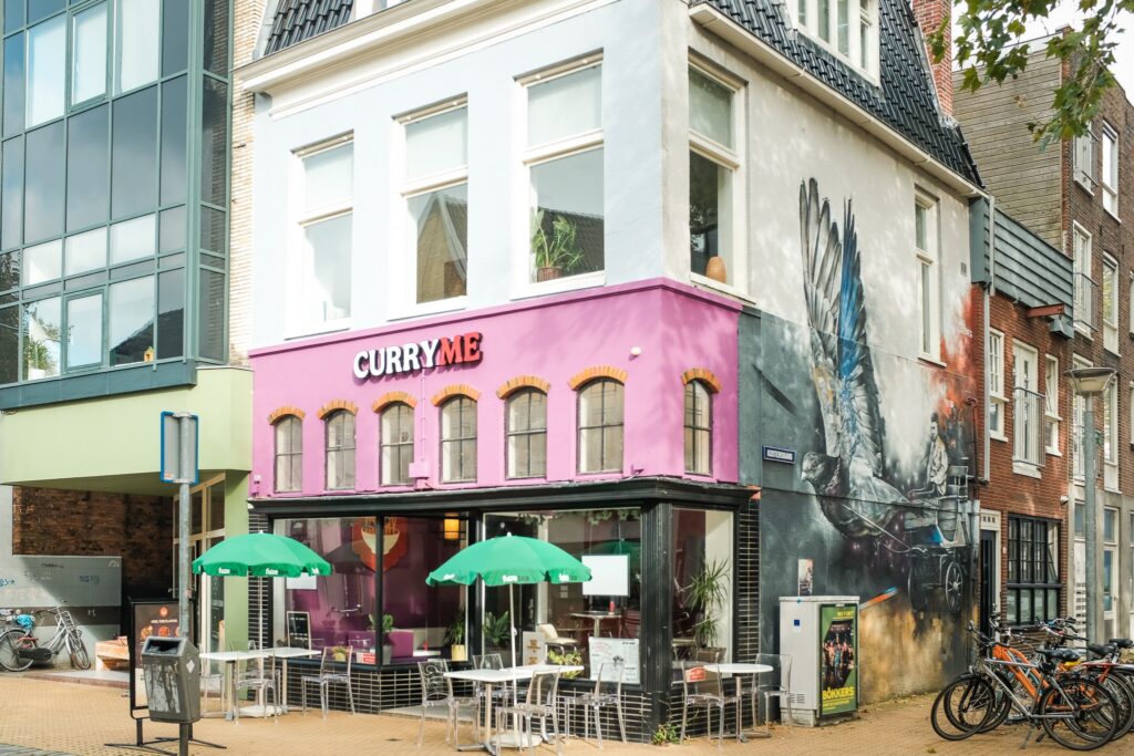 Het roze hoekpand van Curry Me aan de Rademarkt met terras en muurschildering