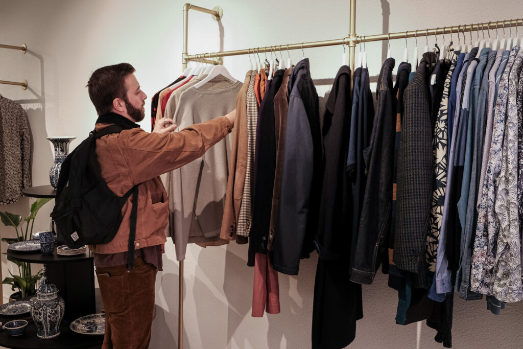 Een man bekijkt tweedehands kleding aan de messing kledingrekken bij Felicità in Groningen