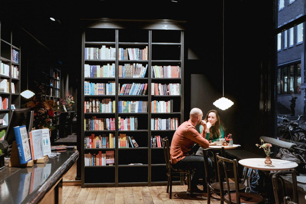 Een stel aan tafel voor een hoge boekenwand in Koffiestation Books & Coffee in Groningen