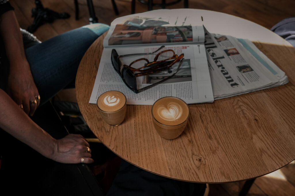 Twee glazen koffie, een krant en brillen op tafel bij Koffiestation Books & Coffee in Groningen