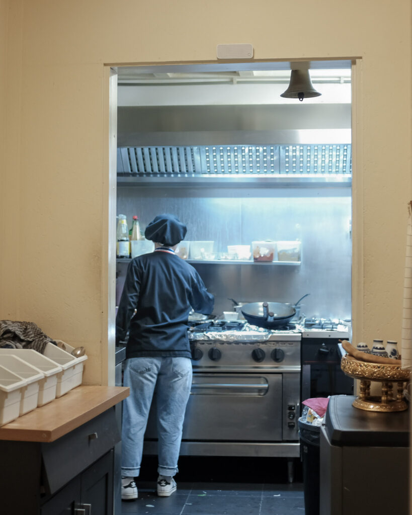 Een kok aan het werk bij het fornuis, gezien door de keukendoorgang