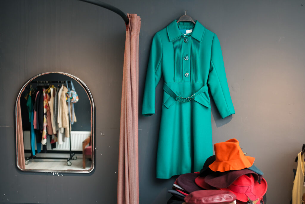 Een groene jurk bij een spiegel en een stapel kleurrijke hoeden
