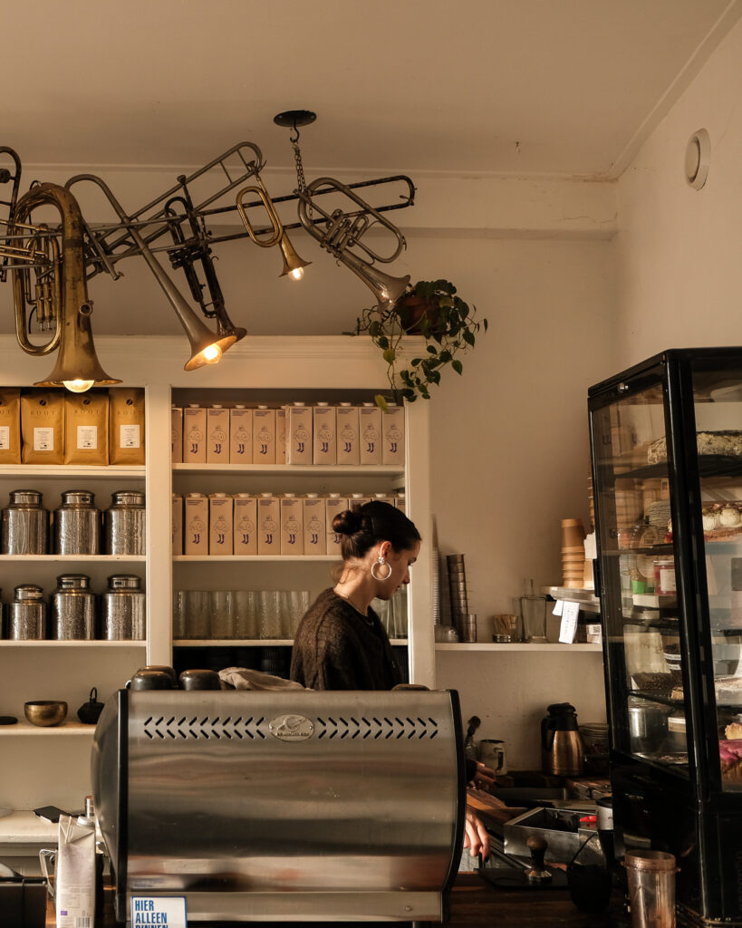Een medewerker van Mahalo werkt achter de espressomachine onder lampen van oude blaasinstrumenten