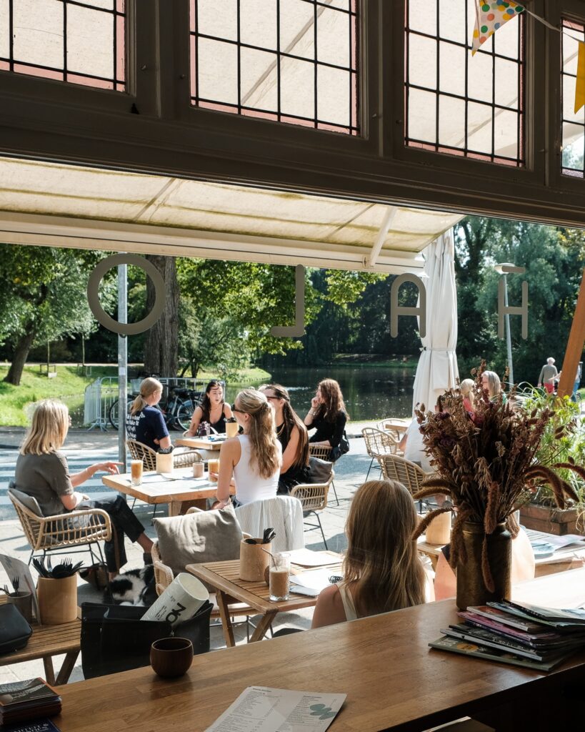 Gasten op het zonnige terras van Mahalo, gezien door het grote raam