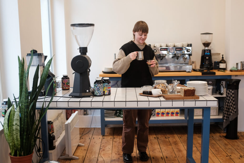 Een barista schenkt koffie in achter de betegelde bar van Revista