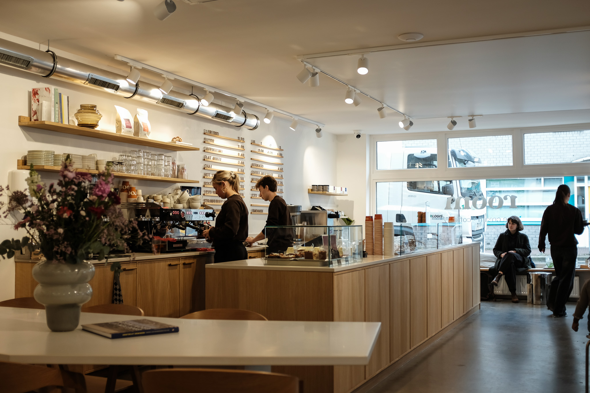 Het lichte interieur van Room met de houten toonbank, bloemen, medewerkers en gasten