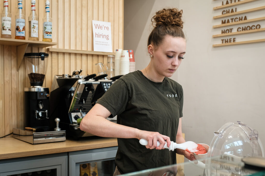 Een medewerker van Room schept roze ijs uit de ijsvitrine