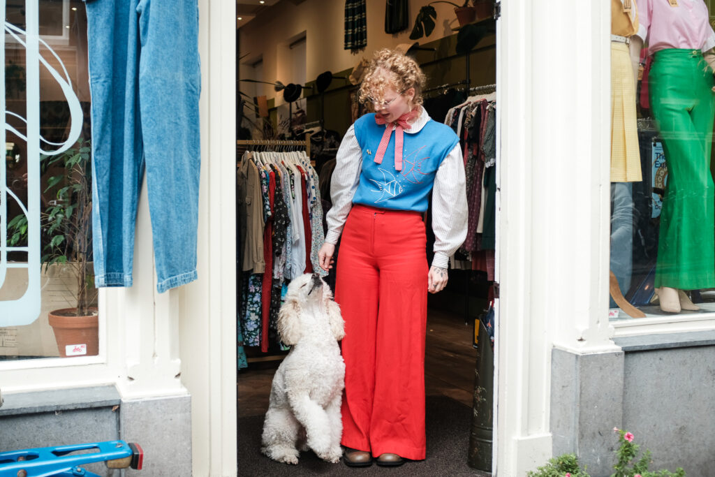De eigenaar van Sappho in een kleurrijke vintage outfit met haar hond voor de winkel