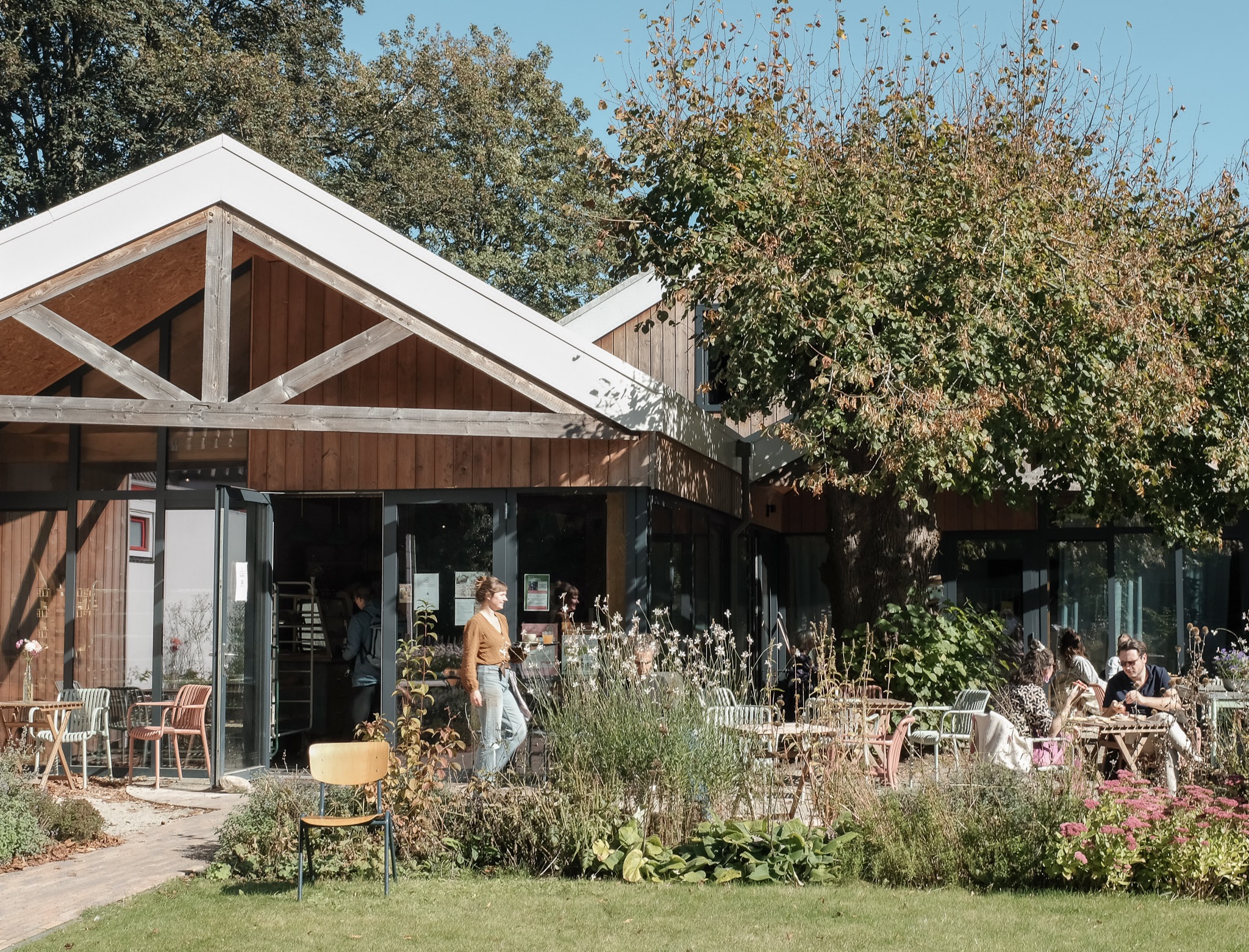 Het houten pand van Stoet in Glimmen met een tuin, een gele stoel en gasten op het zonnige terras