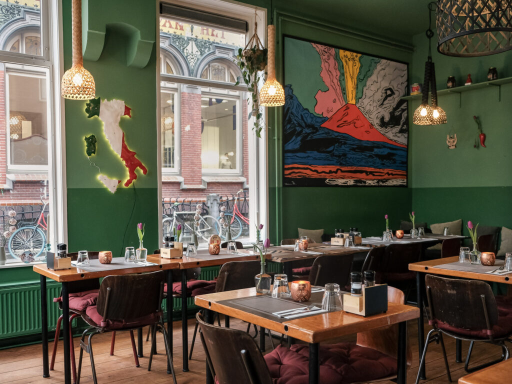 Het groene interieur van Tarantè 081 met gedekte tafels en een kleurrijke vulkaanwand